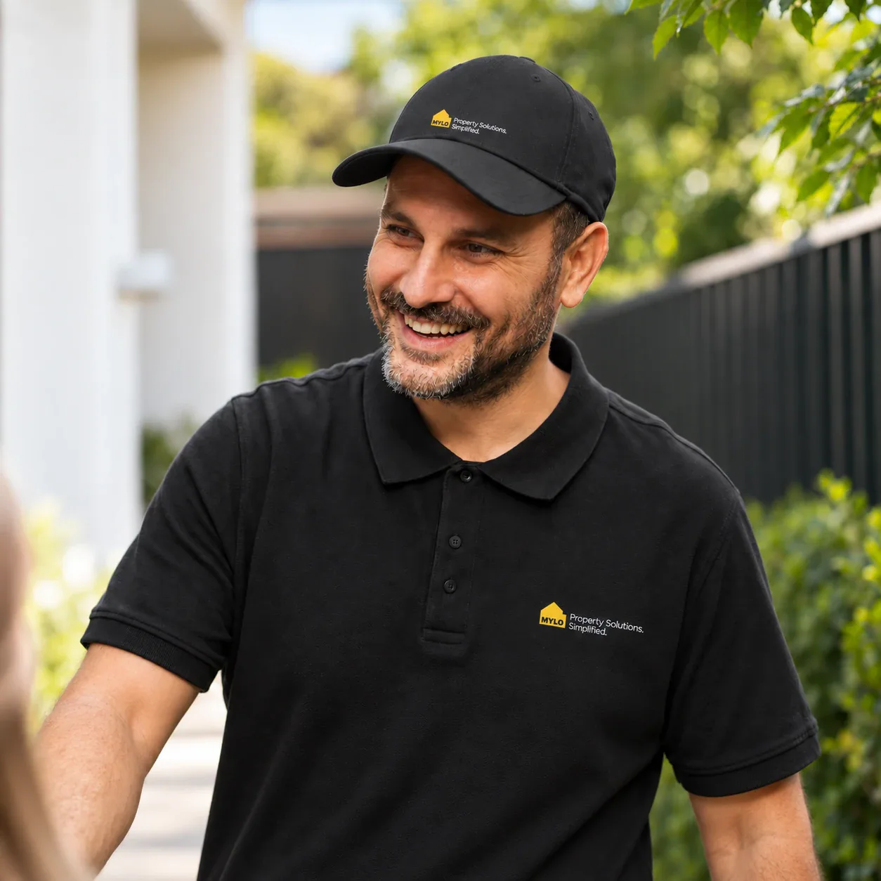 Smiling MYLO technician in a black branded uniform outside a home